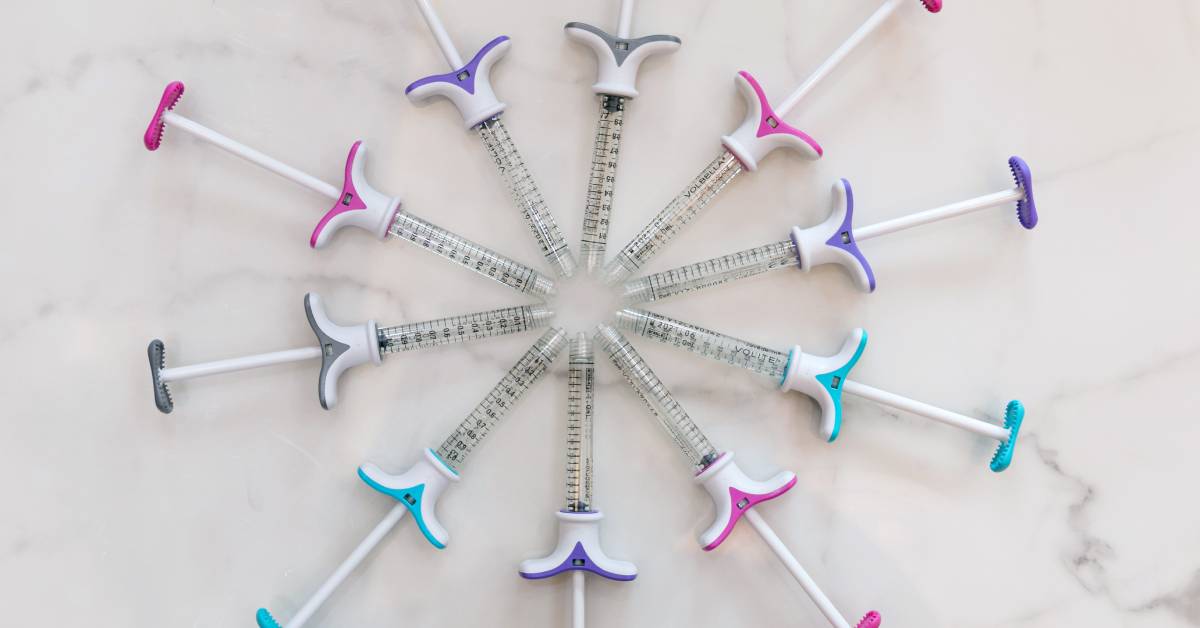 a series of syringes filled with Juvederm arranged in a circle with their tips pointing toward each other